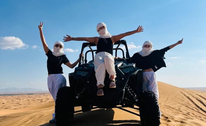 Three people donning white masks maneuver an ATV through the desert, highlighting a thrilling outdoor experience.