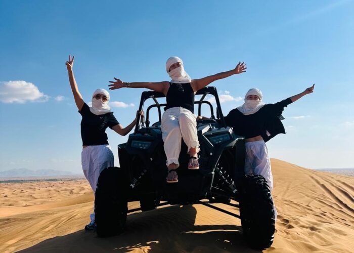 Three people donning white masks maneuver an ATV through the desert, highlighting a thrilling outdoor experience.