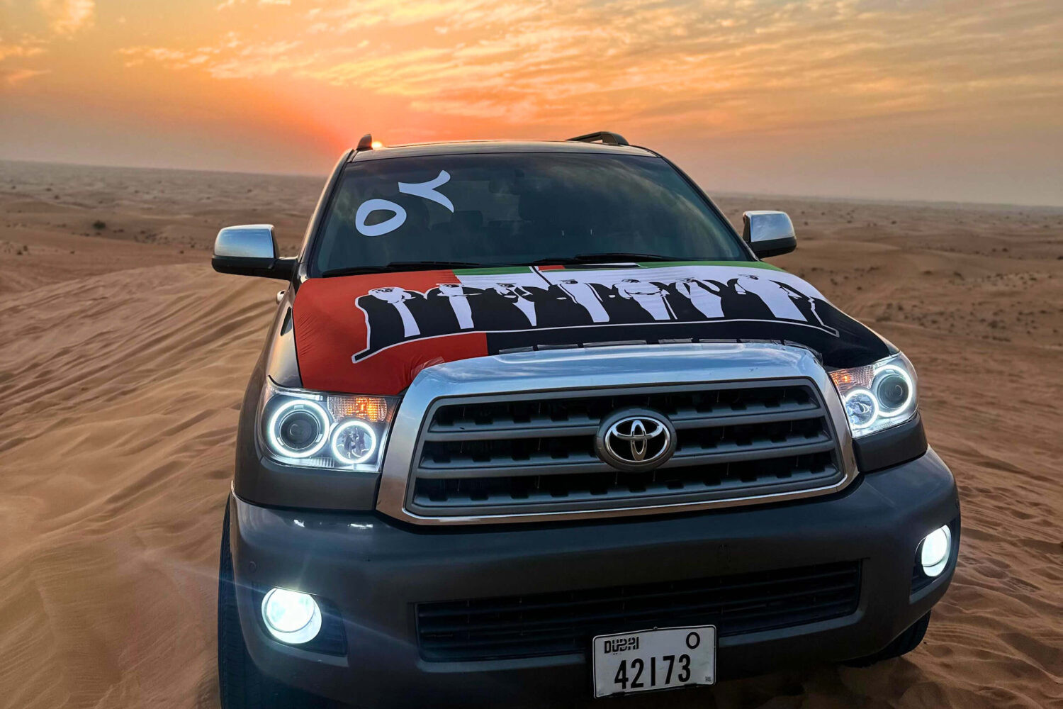 A Toyota car with a UAE flag on the back parked in a desert landscape under blue sky