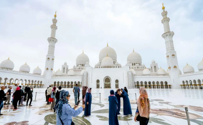 a group of people in front of a large white building with Sheikh Zayed Mosque in the background