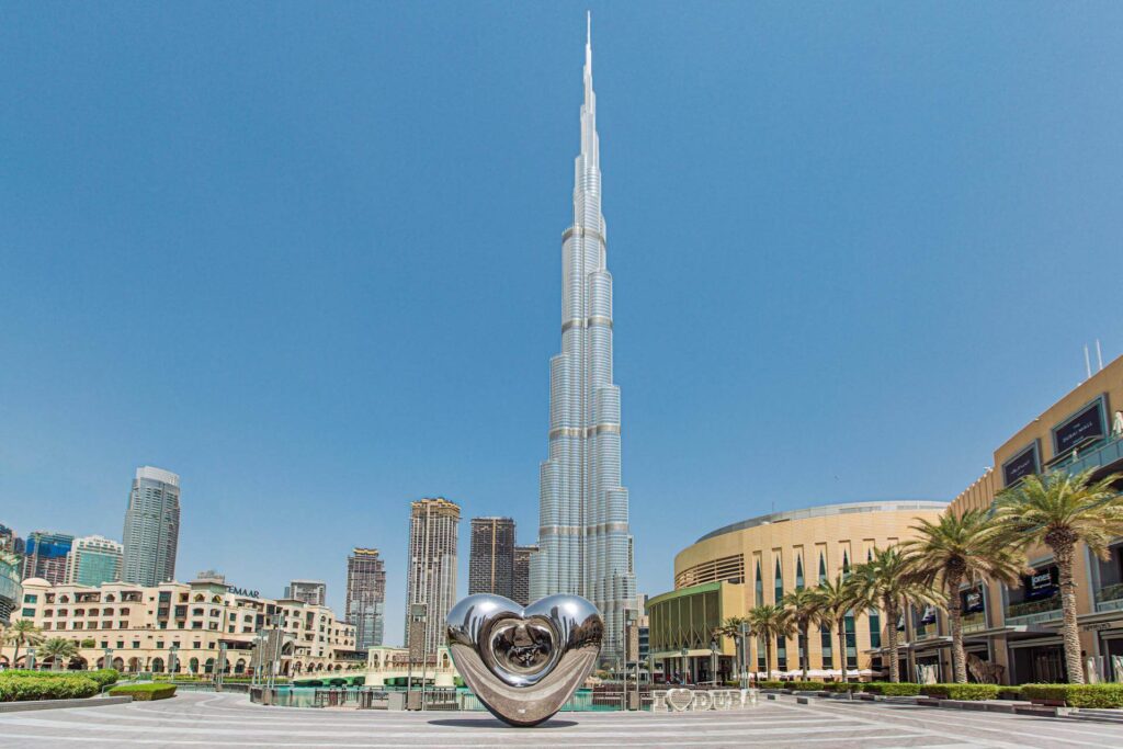 a large silver heart shaped sculpture in front of a tall building