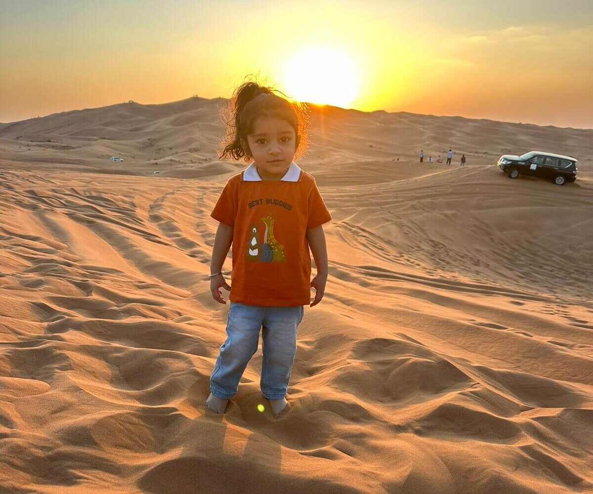 A little girl stands in the sand at sunset