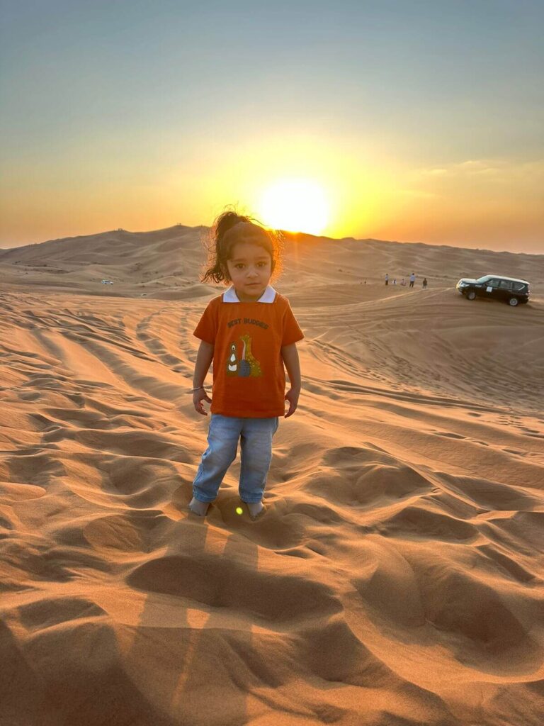 A little girl stands in the sand at sunset