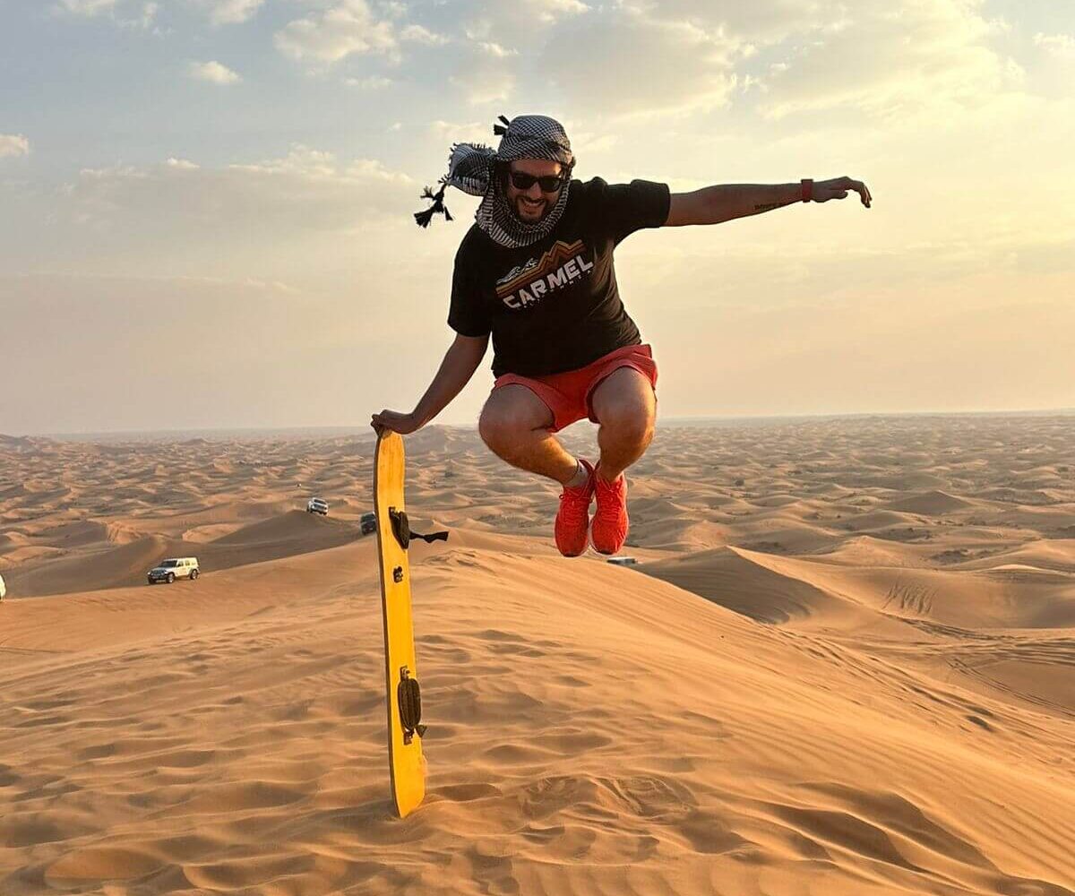 A man leaps over a sand dune with sandboard