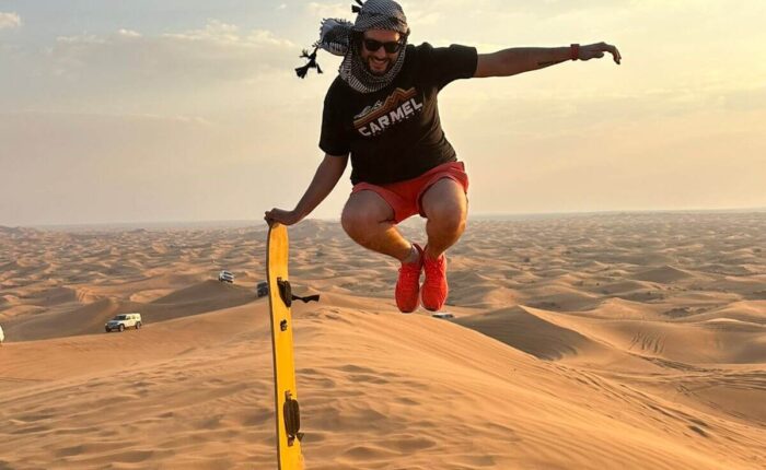 A man leaps over a sand dune with sandboard