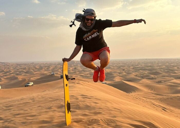 A man leaps over a sand dune with sandboard