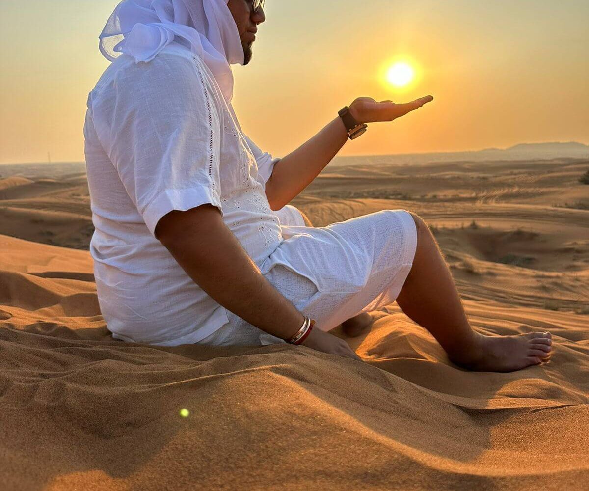 A man wearing white sits in the desert