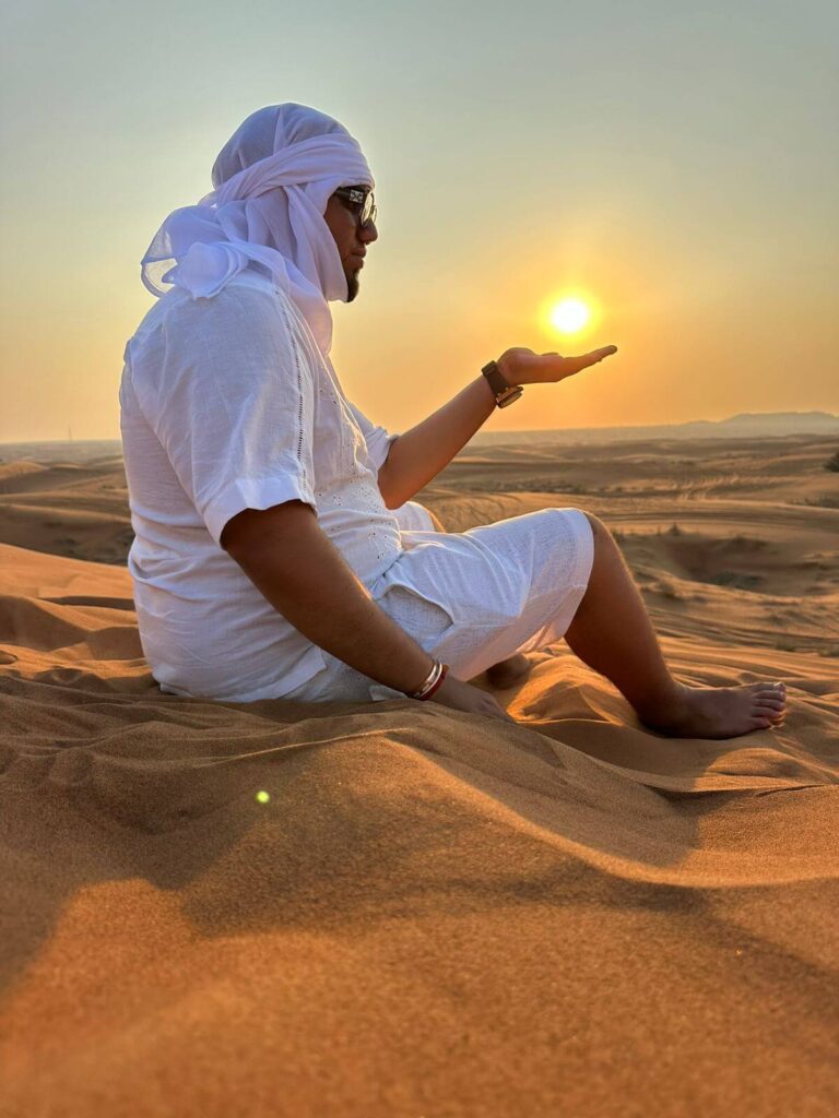 A man wearing white sits in the desert