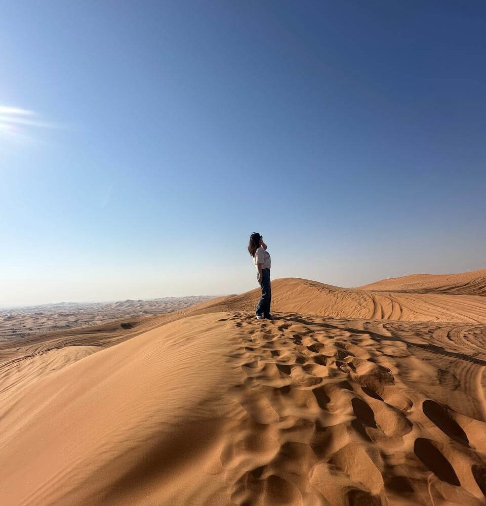 Stands on a sand dune, enjoying the desert view