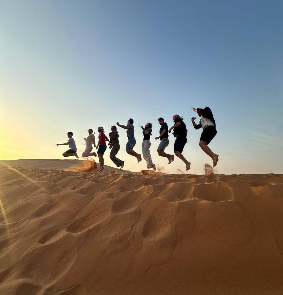 group of people jumping in the desert during sunset